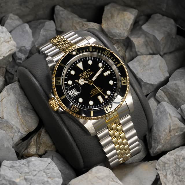 Image of a silver wristwatch with golden details, with a black clock face and white hour markers.