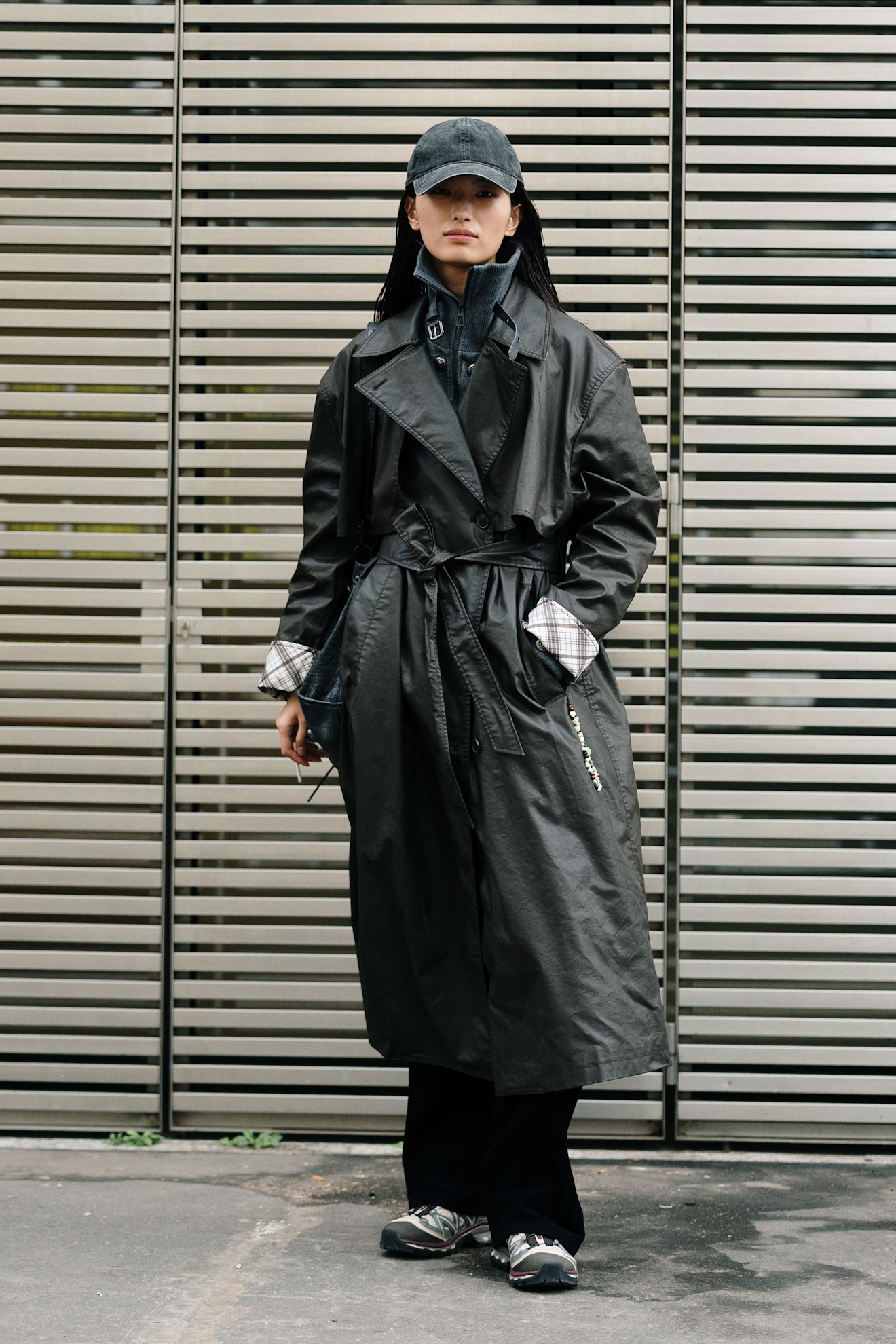 A woman wearing a black leather belted trench coat along with a stylish baseball cap