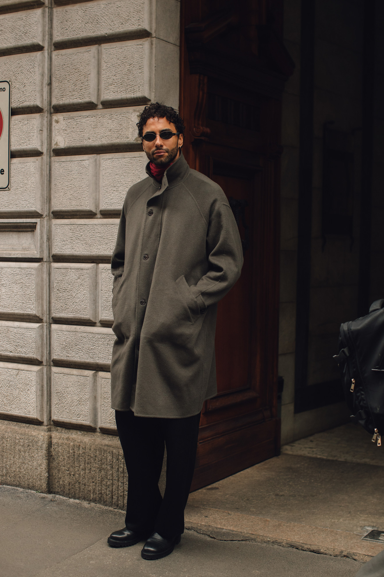 A man wearing a grey green single breasted trench coat in a technical fabric