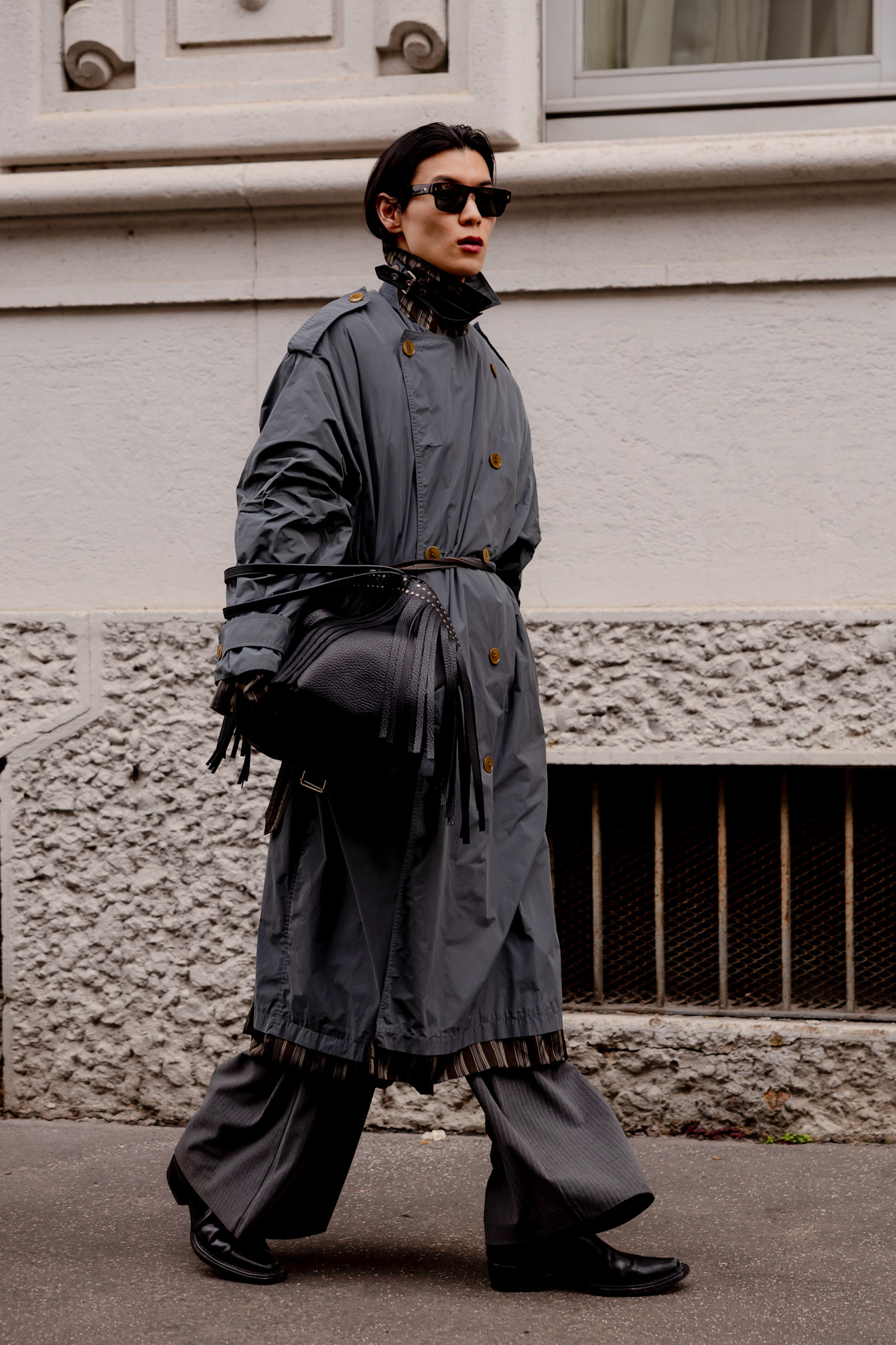 A man wearing a grey double-breasted nylon trench coat and sunglasses